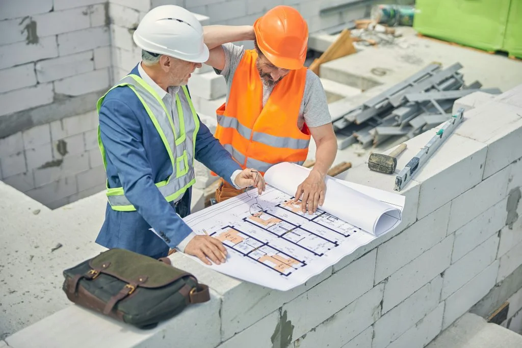 Dva stavební pracovníci kontrolují projektovou dokumentaci na stavbě